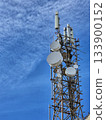 A large communication tower (communication tower) with numerous antennas and satellite dishes, photographed against a bright blue sky. 133900152