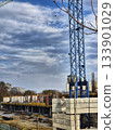 The image is dominated by the tall, blue section of a tower crane in the foreground, a typical feature of any large construction site. 133901029