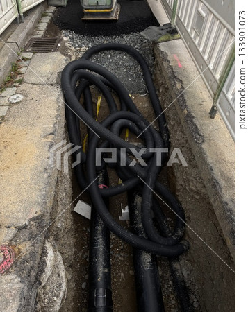 Black pipe is laying on the ground next to a trench 133901073