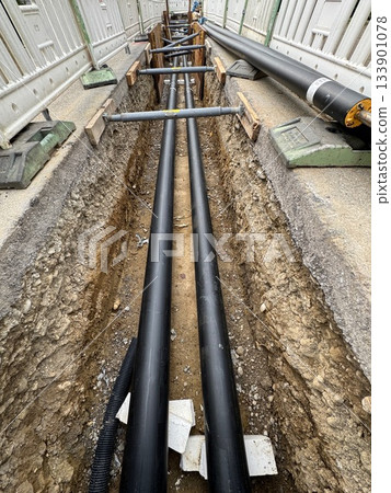 Black pipe is laying in the ground next to a white pipe Black pipe is laying in the ground next to a white pipe 133901078