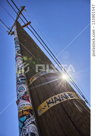Telephone Pole With Stickers and Sunburst Against Blue Sky Perspective View Telephone Pole With Stickers and Sunburst Against Blue Sky Perspective View 133901547