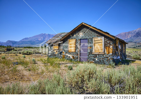 Abandoned House in Desert Field with Mountain Backdrop under Clear Blue Sky Abandoned House in Desert Field with Mountain Backdrop under Clear Blue Sky 133901951