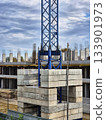 A construction site features a tower crane s blue steel lattice mast with concrete counterweights at the base.  133901973