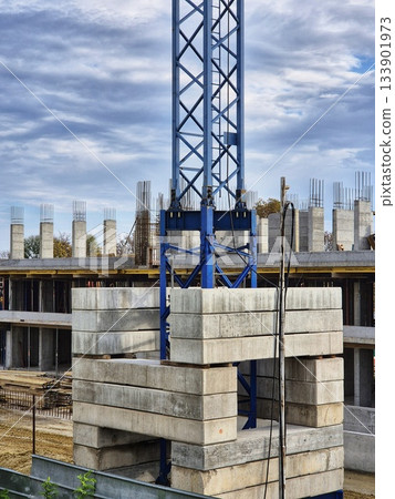 A construction site features a tower crane s blue steel lattice mast with concrete counterweights at the base.  133901973