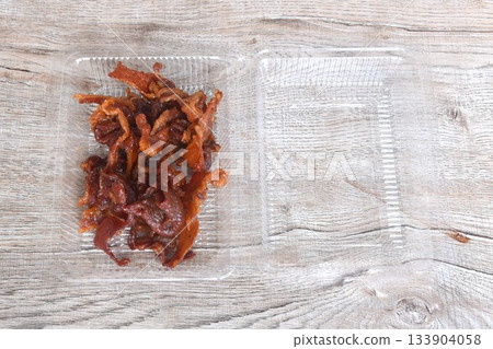salty and sweet dry fried slice pork meat fermenting in soy sauce on transparent plastic packaging box 133904058