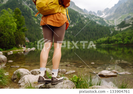 Travel Slovakia, Europe. Tourist with a yellow backpack stands against the backdrop of alpine lake. 133904761
