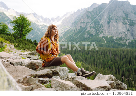 Young traveler woman with a yellow backpack on a cliff. Sports concept, traveler. Active lifestyle. 133904831
