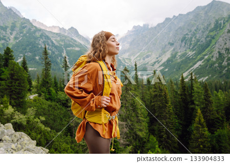 Young traveler woman with a yellow backpack on a cliff. Sports concept, traveler. Active lifestyle. 133904833