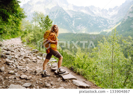 Young traveler woman with a yellow backpack on a cliff. Sports concept, traveler. Active lifestyle. 133904867