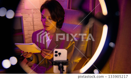 Woman reading notes while filming educational video on phone Woman reading notes while filming educational video on phone 133905217