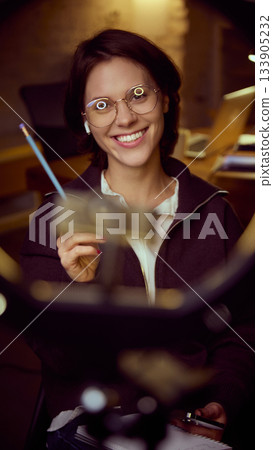 Woman smiling through ring light while explaining material in online session. 133905232