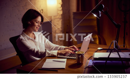 Woman typing on laptop during relaxed evening work session. Woman typing on laptop during relaxed evening work session. 133905237