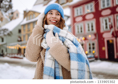 Happy woman in winter clothes walks on the street. Light all around. Winter holidays. 133905302