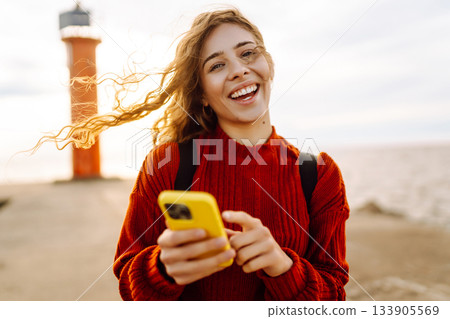 Young woman smiling and using her smartphone at the beach sunset. Blogging, communication concept. 133905569