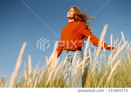Happy woman enjoying nature outdoors in tall grass. Flying hairs. Outdoor. Fashion style. 133905573