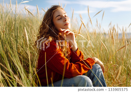 Happy woman enjoying nature outdoors in tall grass. Flying hairs. Outdoor. Fashion style. 133905575