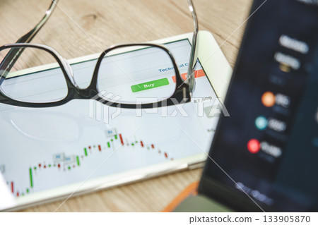Glasses resting on tablet displaying stock market chart and buy button 133905870