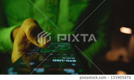 Person checking stock market data on smartphone at night Person checking stock market data on smartphone at night 133905878