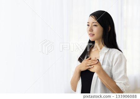 一位女子微笑地倚在窗邊，一手放在胸口。 133906088