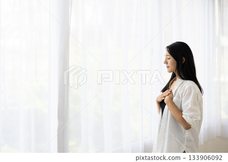 A woman smiling by the window with her hand on her chest A woman smiling by the window with her hand on her chest 133906092
