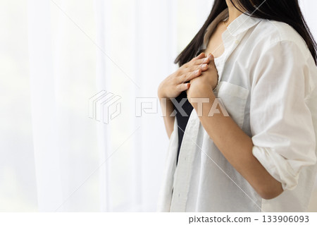 A woman smiling by the window with her hand on her chest A woman smiling by the window with her hand on her chest 133906093
