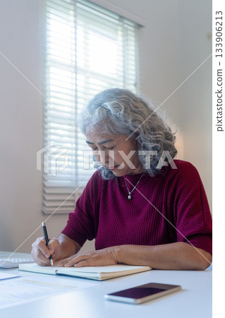 Senior Woman Reviewing Documents and Taking Notes at Home Senior Woman Reviewing Documents and Taking Notes at Home 133906213