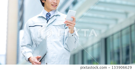 A man in work clothes operating a smartphone at the site 133906629