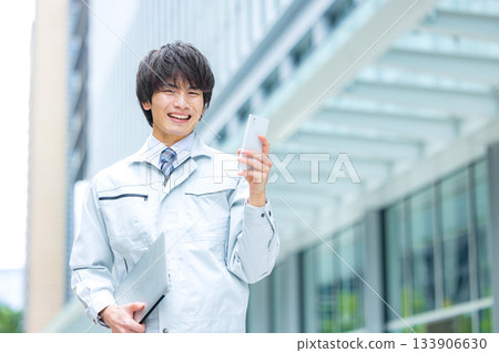 一名身穿工作服的男子正在現場操作智慧型手機 一名身穿工作服的男子正在現場操作智慧型手機 133906630