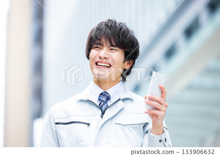 A man in work clothes operating a smartphone at the site A man in work clothes operating a smartphone at the site 133906632