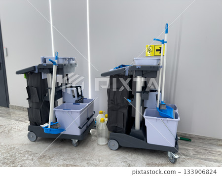 Cleaning carts with cleaning supplies, mops, and buckets. Mobile cleaning cart for maintaining cleanliness of busy public building. Professional cleaning concept Cleaning carts with cleaning supplies, mops, and buckets. Mobile cleaning cart for maintaining cleanliness of busy public building. Professional cleaning concept 133906824