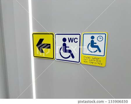 Set of signs for people with disabilities on wall. Arrow points to accessible restroom and to waiting area with braille text. Directional navigation for people with mobility issues Set of signs for people with disabilities on wall. Arrow points to accessible restroom and to waiting area with braille text. Directional navigation for people with mobility issues 133906830