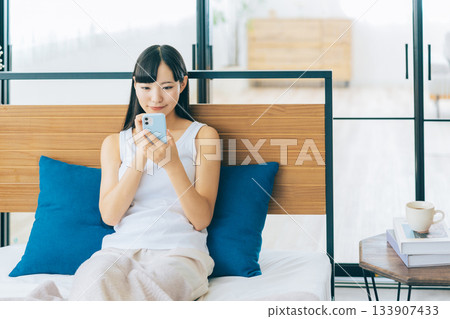 少婦在床上的看智能手機 133907433
