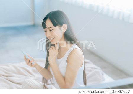 少婦在床上的看智能手機 133907697