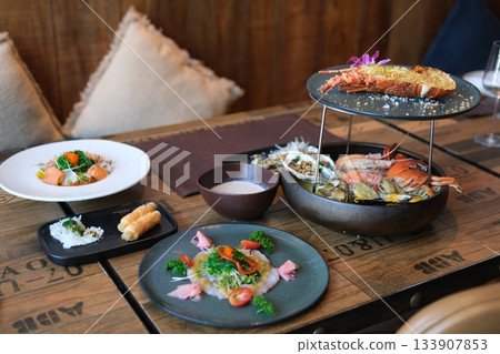 Seafood platter with lobster, shrimp, mussels on ice with lemon in restaurant setting. Fresh salad, seafood pasta, creamy sauce on wooden table. Elegant dining experience, gourmet cuisine concept. Seafood platter with lobster, shrimp, mussels on ice with lemon in restaurant setting. Fresh salad, seafood pasta, creamy sauce on wooden table. Elegant dining experience, gourmet cuisine concept. 133907853