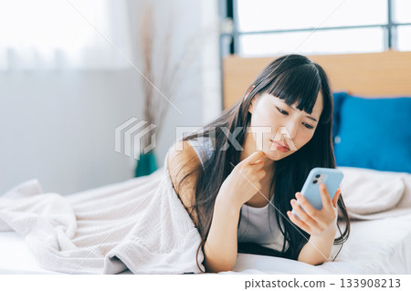 一位女士躺在床上看著手機，心情很低落。 133908213