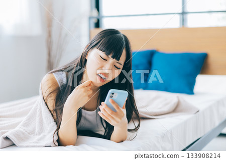 一位女士躺在床上看著手機，心情很低落。 133908214