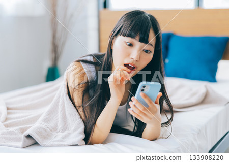 Young woman looking at smartphone in bed 133908220