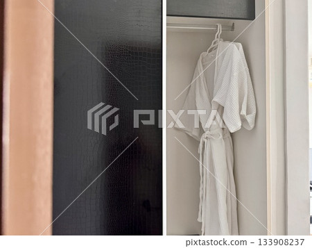 A clean white waffle bathrobe is hanging on a hanger in the hotel closet A clean white waffle bathrobe is hanging on a hanger in the hotel closet 133908237