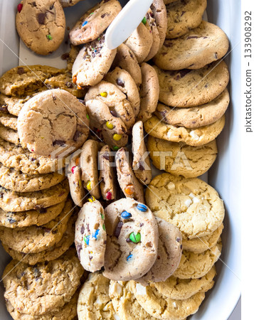 Assortment of cookies including chocolate chip and sprinkle cookies displayed in a white ceramic tray. The image is well-lit and shot from above. Assortment of cookies including chocolate chip and sprinkle cookies displayed in a white ceramic tray. The image is well-lit and shot from above. 133908292