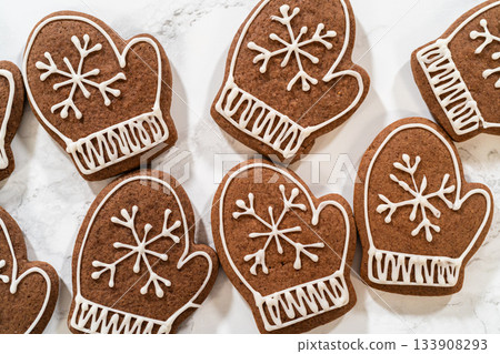 Close-up of beautifully decorated mitten-shaped gingerbread cookies featuring intricate white royal icing designs, arranged on a marble surface. Close-up of beautifully decorated mitten-shaped gingerbread cookies featuring intricate white royal icing designs, arranged on a marble surface. 133908293
