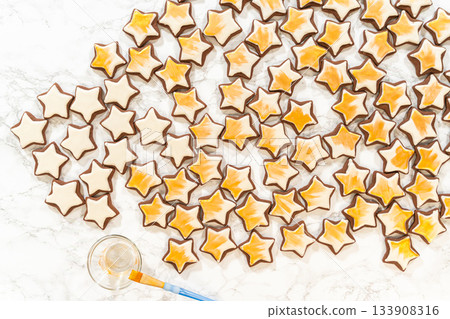 An artistic top-down arrangement of gingerbread star cookies decorated with royal icing, with gold luster dust adding a glamorous finish to these festive treats. 133908316