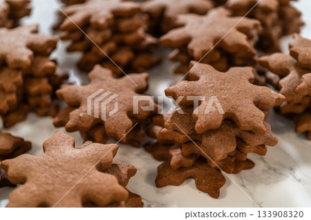 Side view of chocolate ginger snowflake cookies piled together on a parchment-lined surface, showcasing their festive design and holiday charm. Side view of chocolate ginger snowflake cookies piled together on a parchment-lined surface, showcasing their festive design and holiday charm. 133908320