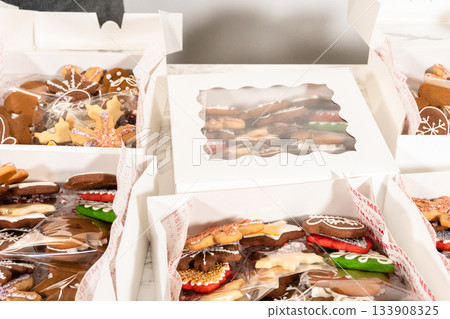 Seen from a medium perspective, gloved hands arrange a variety of gingerbread cookies inside divided holiday gift boxes. The festive assortment features intricate icing designs and bright holiday Seen from a medium perspective, gloved hands arrange a variety of gingerbread cookies inside divided holiday gift boxes. The festive assortment features intricate icing designs and bright holiday 133908325