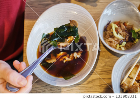 Person enjoying bowl of traditional japanese miso soup with ingredients 133908331