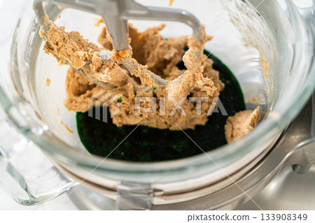 The creamed butter and sugar mixture being combined with the vibrant green maple syrup blend in the mixer for Vibrant Green Gingerbread Cookies for Festive Baking. 133908349
