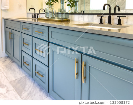 Detail view of a blue bathroom vanity with brass drawer handles. The vanity is topped with a light surface and features clean, modern lines. Detail view of a blue bathroom vanity with brass drawer handles. The vanity is topped with a light surface and features clean, modern lines. 133908372
