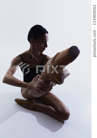 Ballerina seated on floor stretching raised leg while holding foot Ballerina seated on floor stretching raised leg while holding foot 133909002