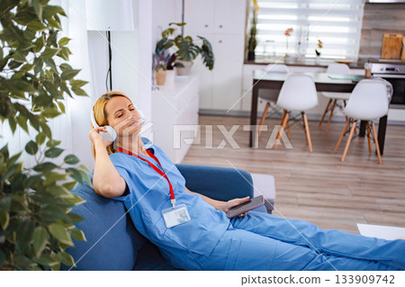 Female doctor relaxing on sofa listening to music with headphones after work 133909742