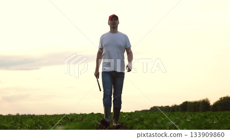 Agriculture, Modern agriculture scene with man exploring potential of his harvest, Young man working outdoors on sustainable farm under calm sky, Dedicated farmer assessing soil quality and crop 133909860