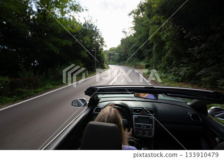 Young woman driving convertible along scenic ocean coast and mountain road at sunset, carefree summer vacation, travel freedom and adventure on coastal highway 133910479